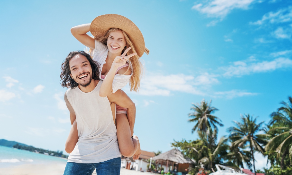 Mujer subida a hombros de su novio en playa de palmeras