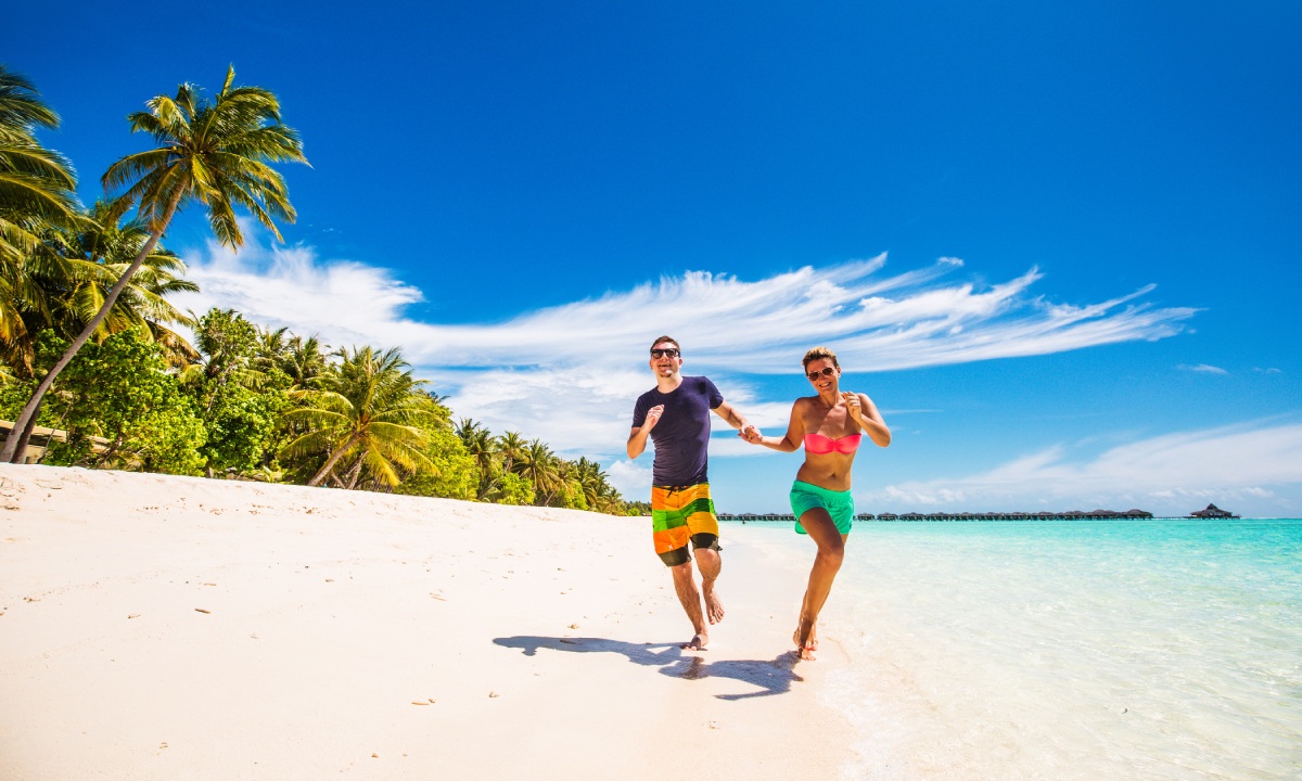 Una pareja corriendo de la mano por la orilla del mar.