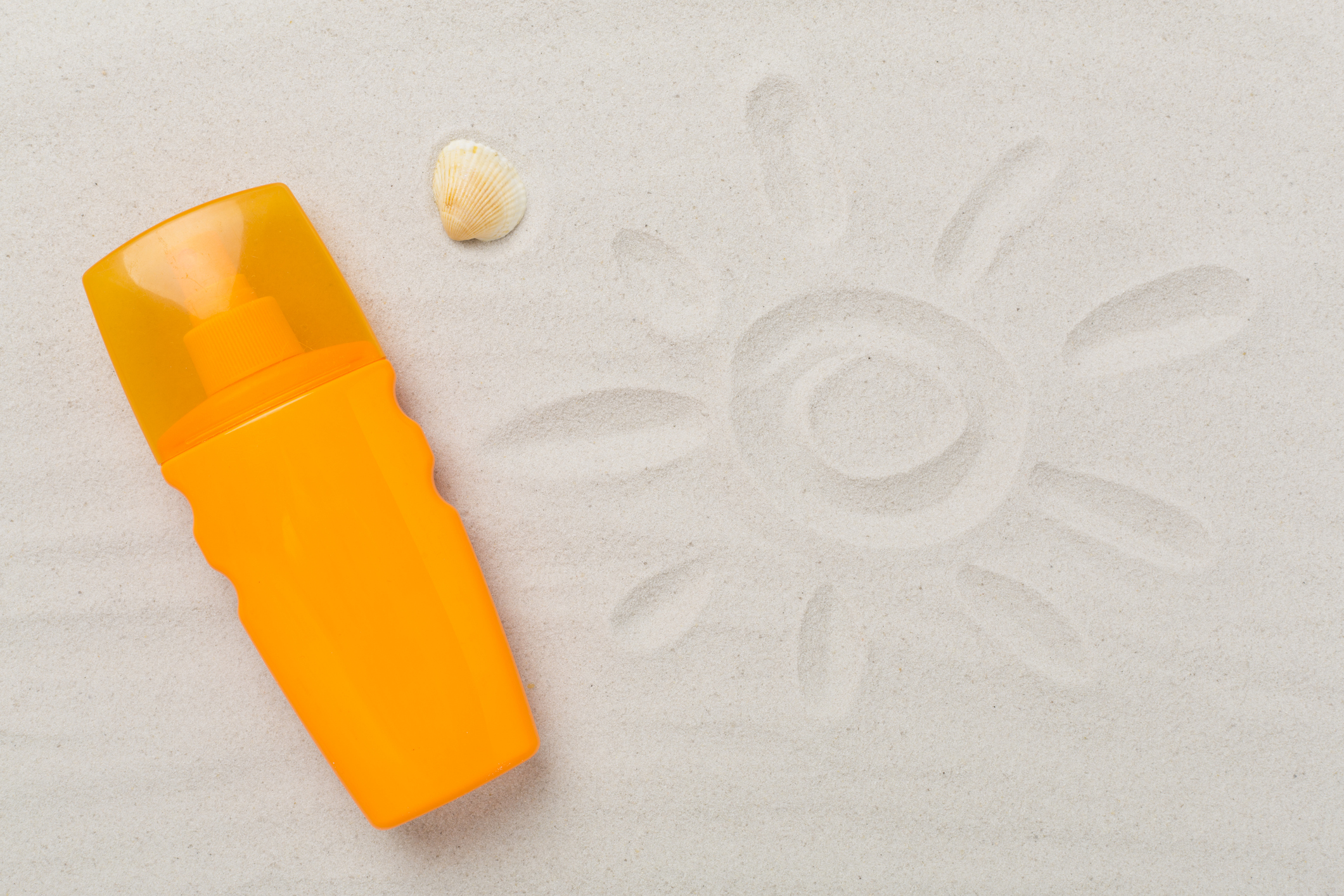 Sonnencreme neben einer in den Sand gemalten Sonne