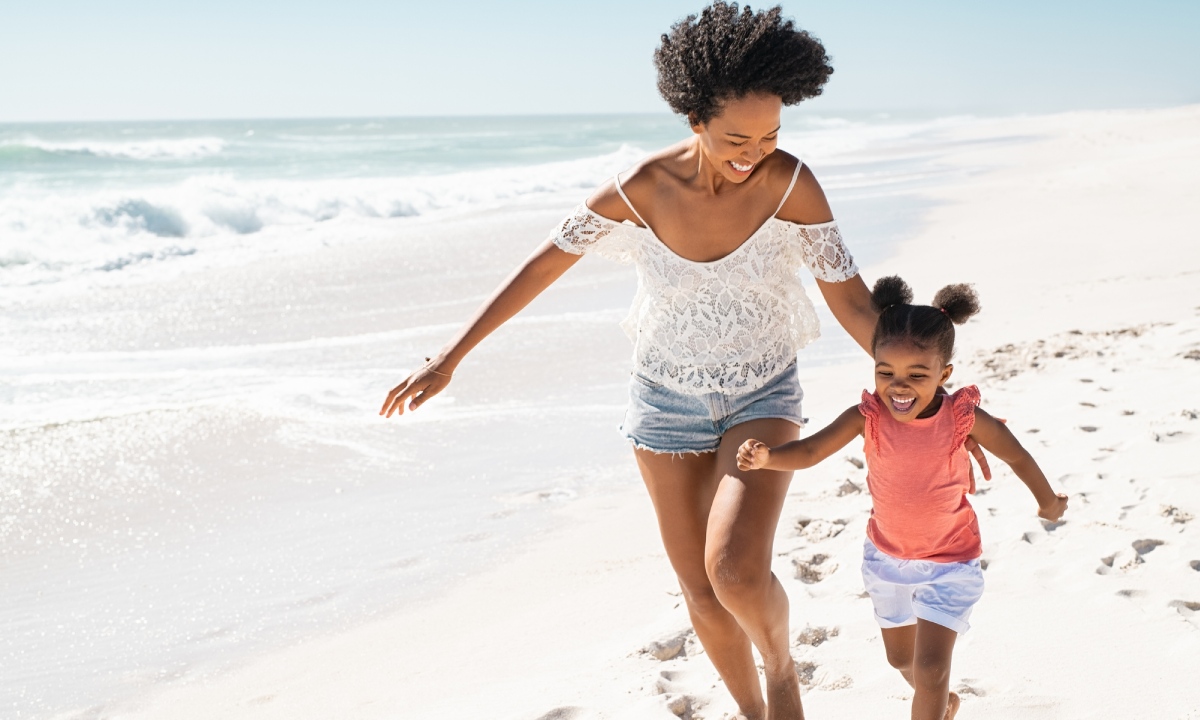 Una mujer y una niña sonriendo mientras corren por la playa.