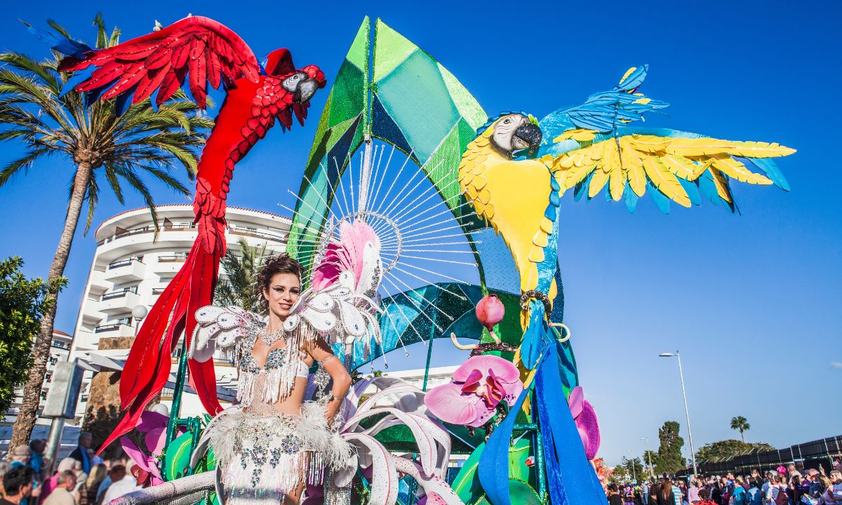 A queen or contestant wearing a colourful parrot-themed fantasy costume on a float at the Las Palmas Carnival in Gran Canaria.