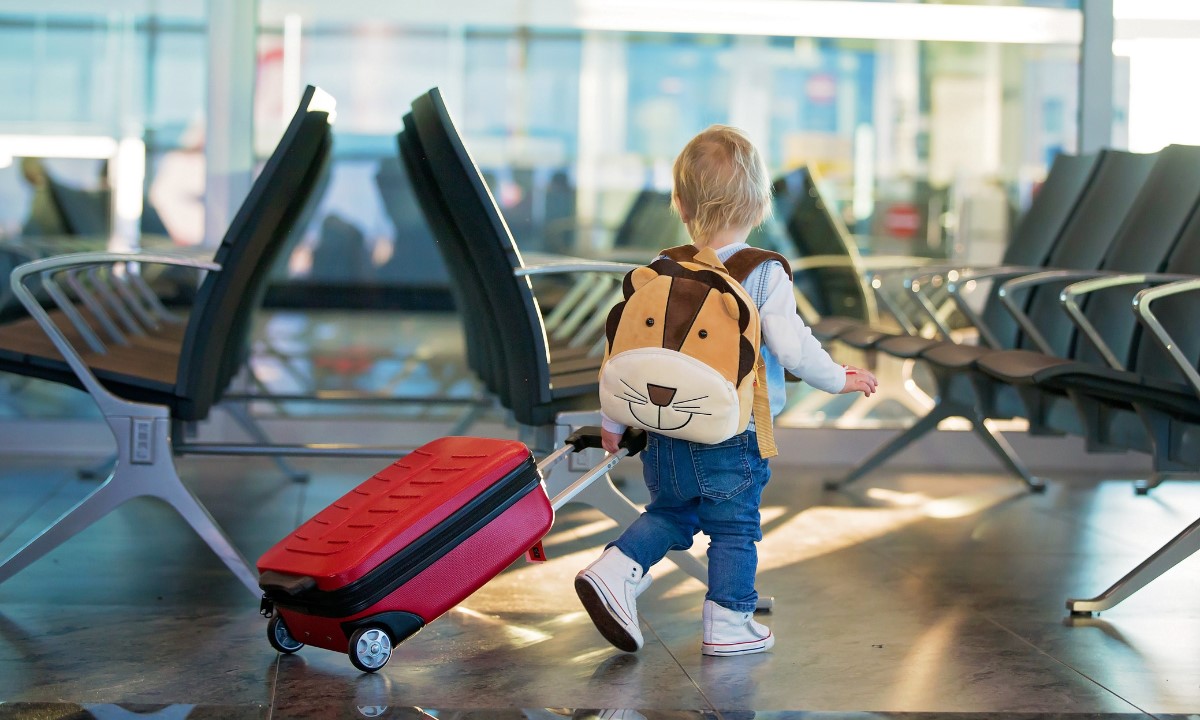 Kind mit Rucksack zieht einen Koffer im Flughafen