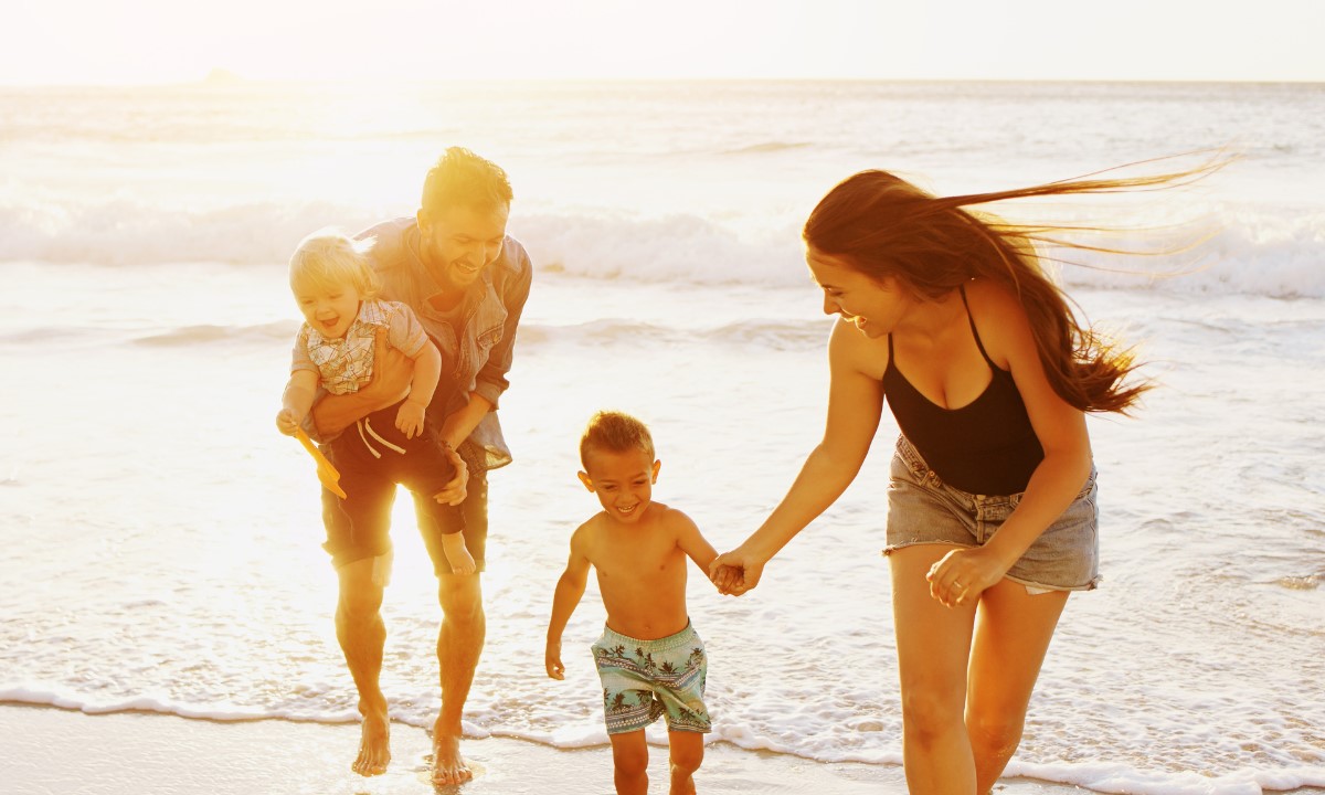 Familie mit Kindern spielt bei Sonnenuntergang am Strand während ihres Familienurlaubs auf den Kanaren