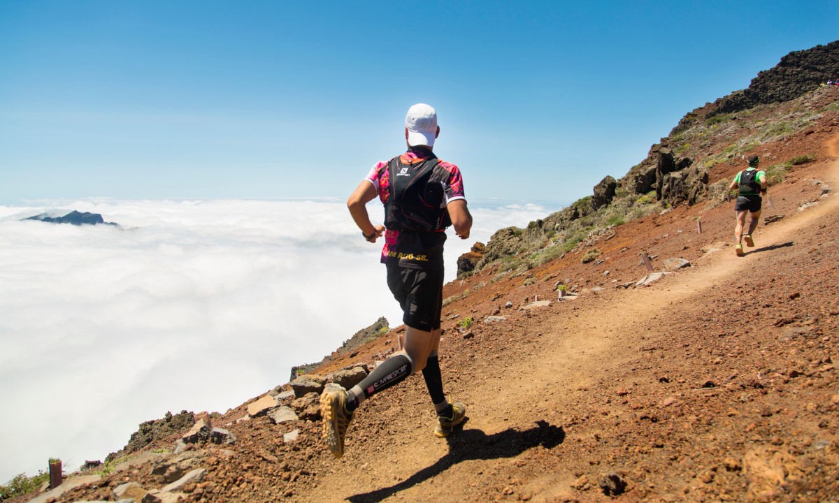 Runners in the Transvulcania ultramarathon on La Palma racing along a mountain trail above a sea of clouds.